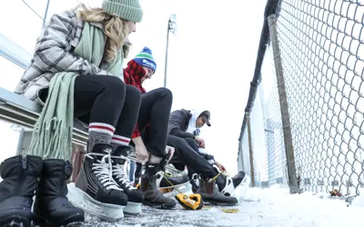 three adults sitting on bench in winter tying their skates