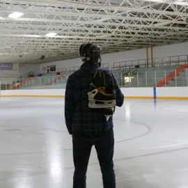 man standing in front of ice rink with skates over shoulder